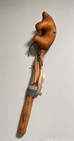 Full view of rattle showing animal head, handle, bead band, and feather tassels