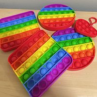 Five rainbow silicone Pop It toys laid out on tabletop