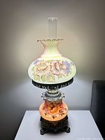 Full view of lamp lit showing upper and lower hand-painted globes, chimney, and metal base