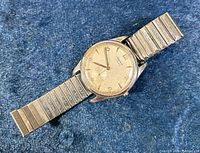 Full view of watch on blue background showing case, dial, and stretch bracelet