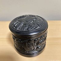 Black resin cylindrical box with lid in place, side carving visible