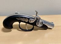 Left side view of pistol lighter showing metal barrel, trigger, hammer, and black grip