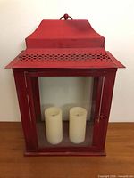Front view of red metal and glass lantern with two pillar candles inside