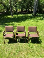 Front view of three brown upholstered wooden armchairs standing on grass