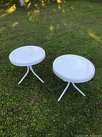 pair of white metal round patio tables on grass
