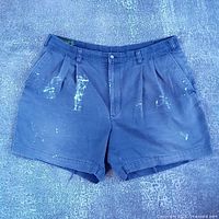 Front view of blue distressed denim shorts with paint splatter