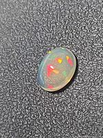 Front view of oval crystal opal showing play-of-color on textured background