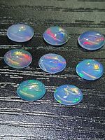 Eight opal cabochons on dark surface showing colour play