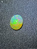 Oval Ethiopian crystal opal displaying multicolor play-of-color on textured black background