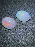Two oval opal cabochons on textured background, showing play of colour