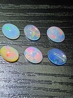 Six oval jelly opal cabochons on dark background showing play of color