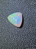 Triangular opal on textured background showing multicolour flashes