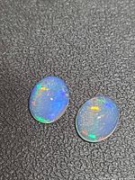 Both oval opals on textured surface, showing body clarity and color play