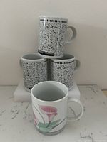 Group of four mugs showing three matching speckled Zellers mugs and one floral Abbott mug