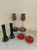 All six candle holders grouped: wood & brass pair at back, green glass pair left front, clear/red hurricane pair right front