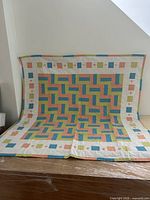Full view of square multicolour patchwork quilt draped over surface