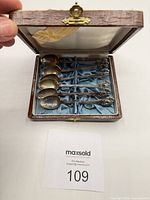 Open case showing six elephant-finial spoons in blue silk interior