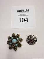 Both brooches front view next to lot number card