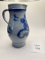 Front view of blue and white lava glazed stoneware pitcher with raised floral pattern