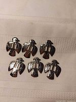 Six silver-tone bird-shaped bolo tie fasteners laid out on fabric