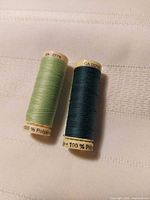 Front view of two Gutermann polyester thread spools showing thread colours light green and dark teal