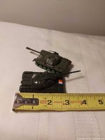 Green and black miniature tanks beside ruler showing length
