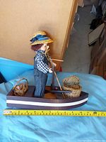 Full view of boy doll in wooden boat with baskets, tape measure for scale
