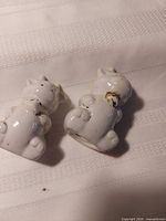 Two white porcelain cow figurine shakers lying on side showing underside and paint wear
