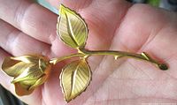 Front view of gold-tone rosebud brooch showing leaves and stem