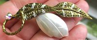 Front view of brooch showing filigree leaf, faux pearl insert, rhinestone loop