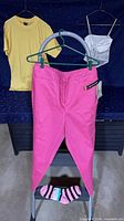 All garments displayed: pants on hanger, tee on backdrop, camisole on hanger, socks on step stool