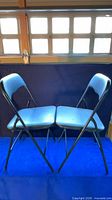 Two black metal folding chairs upright and folded open