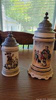 Front view of both steins showing size difference and printed scenes