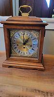 Front view showing ornate dial, Roman numerals, brass handle