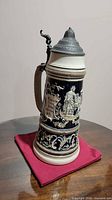 Full left-side view of stein showing figural relief and pewter lid