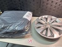 Sealed black quilted car seat cover beside silver hubcap on table
