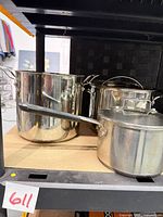 Three stainless steel pots with one lid visible on shelving