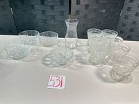 Group shot of all 12 clear pressed glass items: bud vase, six footed dessert glasses, five small bowls