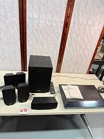All components laid out: main unit, subwoofer, 4 satellites, center speaker, remote, manuals, cables