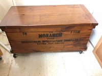 Front view of closed chest showing stencilled text, wood finish and casters