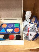 Open wooden box showing puzzle board, loose wooden shapes and numbered spinner tile