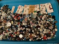 Wide view showing large blue tray filled with hundreds of assorted vintage buttons and a few cards of unused buttons