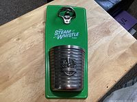 Full view of green metal back plate with opener and cap catcher attached