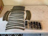 Overall lot showing 23 curved track pieces laid out, clear plastic organizer with wheel parts