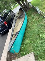 Full view of teal Swift canoe from bow to stern on grass beside vehicle