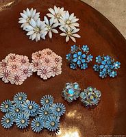 All five pairs of floral clip-on earrings displayed on brown surface