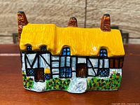 Front view of porcelain cottage showing yellow roof, chimneys, black-and-white timber framing, garden base