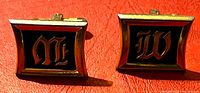 Front view of both cufflinks showing gold-tone frames, black enamel, gothic letters