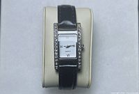 Front view of wristwatch on display cushion showing rectangular case with rhinestones and leather band