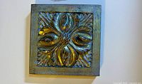 Front view of square plaque showing floral relief and patina finish
